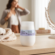 Natura Tododia Leite de Algodão roll-on 70ml em penteadeira com mulher se preparando ao fundo, em cena ilustrativa; acessórios não inclusos