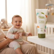 Natura Mamãe e Bebê Hidratante 100ml em destaque com bebê sorridente no colo de um adulto ao fundo, em cena ilustrativa